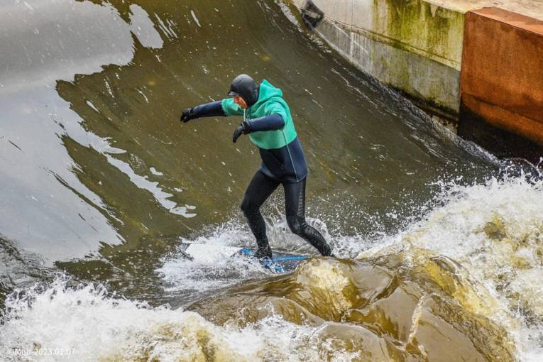 Mann im Neopren-Anzug surft auf der Leinewelle.